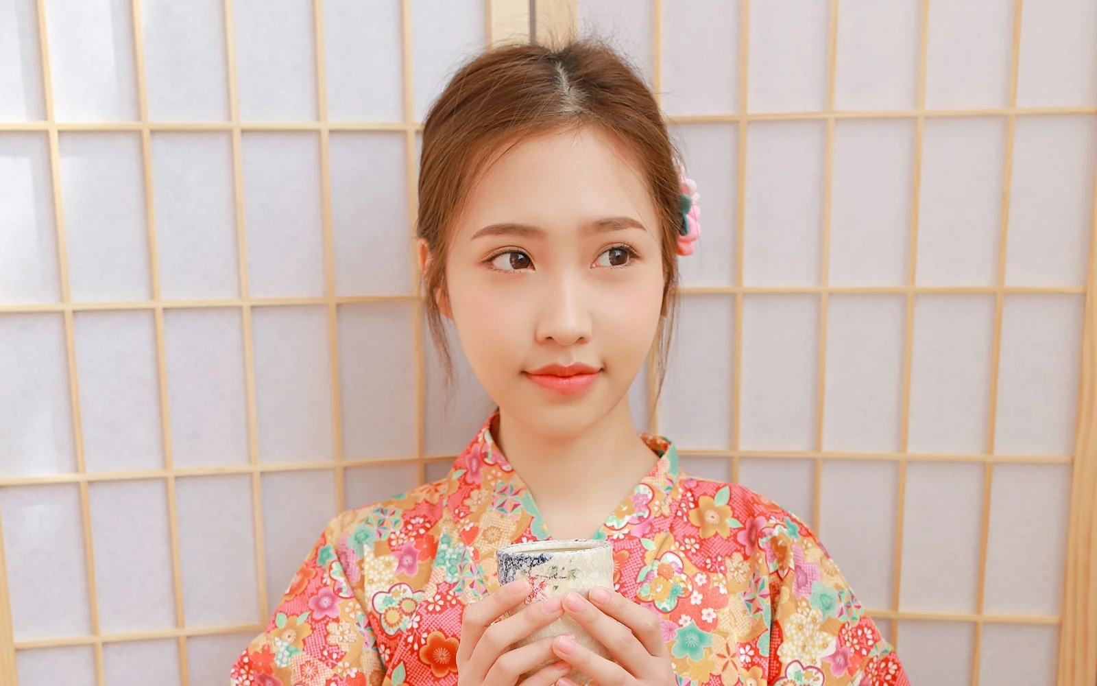 화려한 꽃무늬 옷을 입은 성인 여성이 격자무늬 배경 앞에서 양손으로 휴대전화를 들고 있습니다.