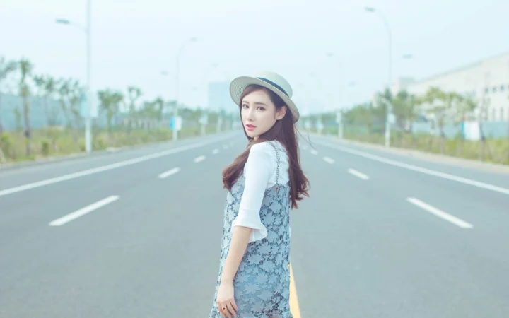 一名戴帽子的女性站在宽阔公路中央回望镜头。