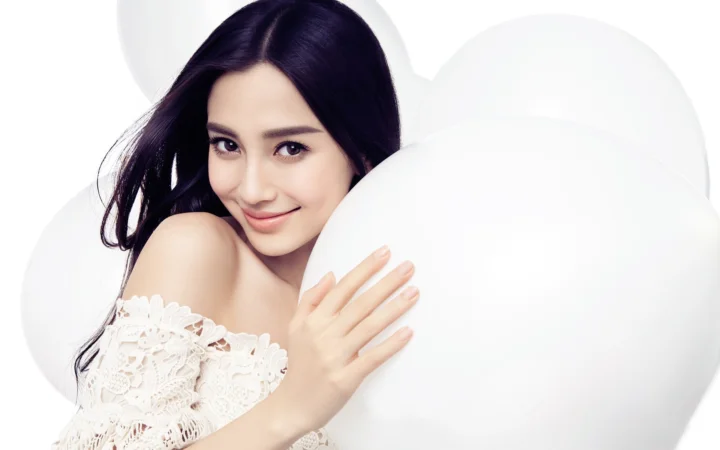 一位长发女性在白色抱枕间微笑面对镜头。