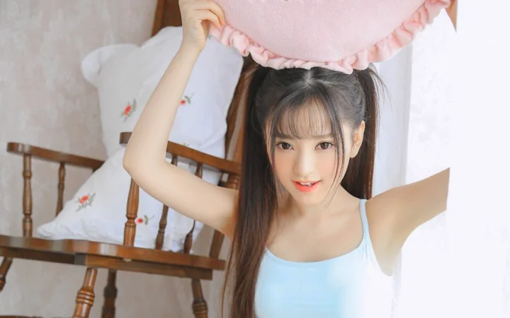 一名身穿浅蓝色上衣的女性在卧室中举着一个粉色枕头。