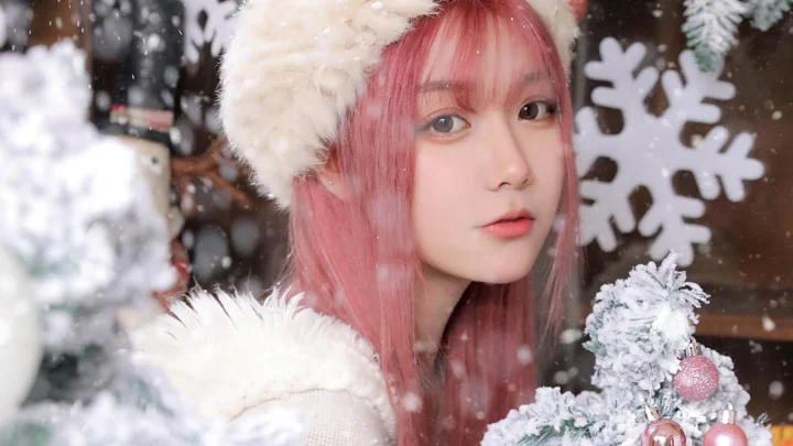 一位粉色长发女子戴着毛绒冬帽，置身于飘雪和圣诞装饰之间。