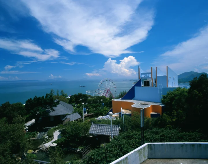 画面展现了蓝色海面、滨海公园、摩天轮、树木和现代建筑。
