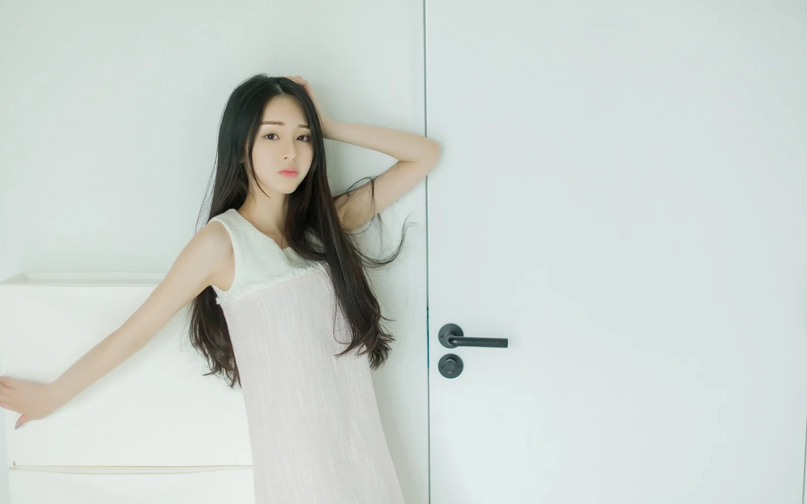 흰색 민소매 원피스를 입은 여성이 흰색 문 옆에서 포즈를 취하고 있습니다.