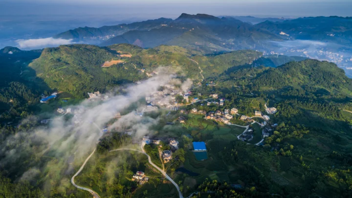 航拍画面展现了群山、云雾缭绕的山村和蜿蜒道路。