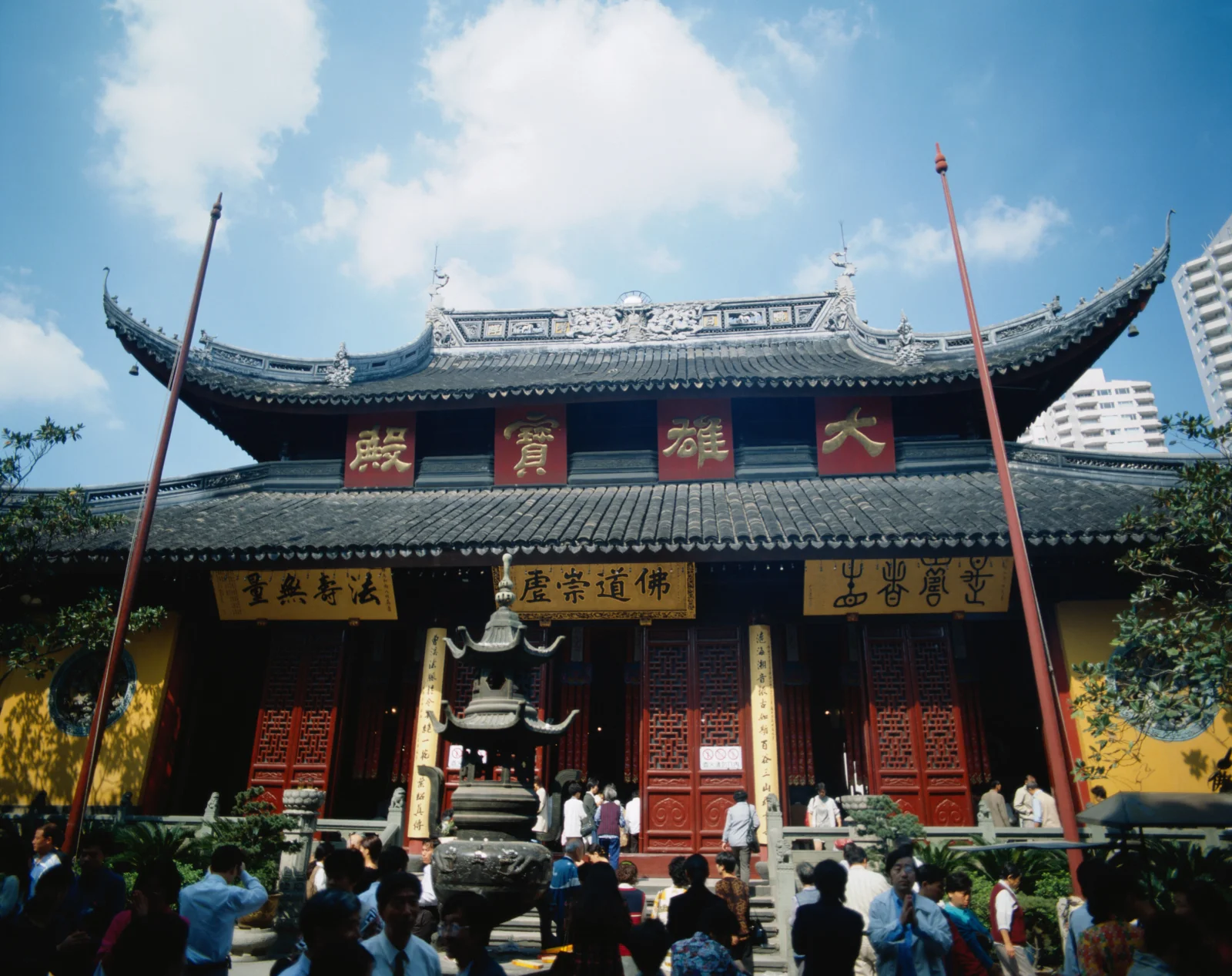 蓝天白云下，一座带有 ornate 屋檐和红色门窗的传统寺庙建筑映入眼帘。