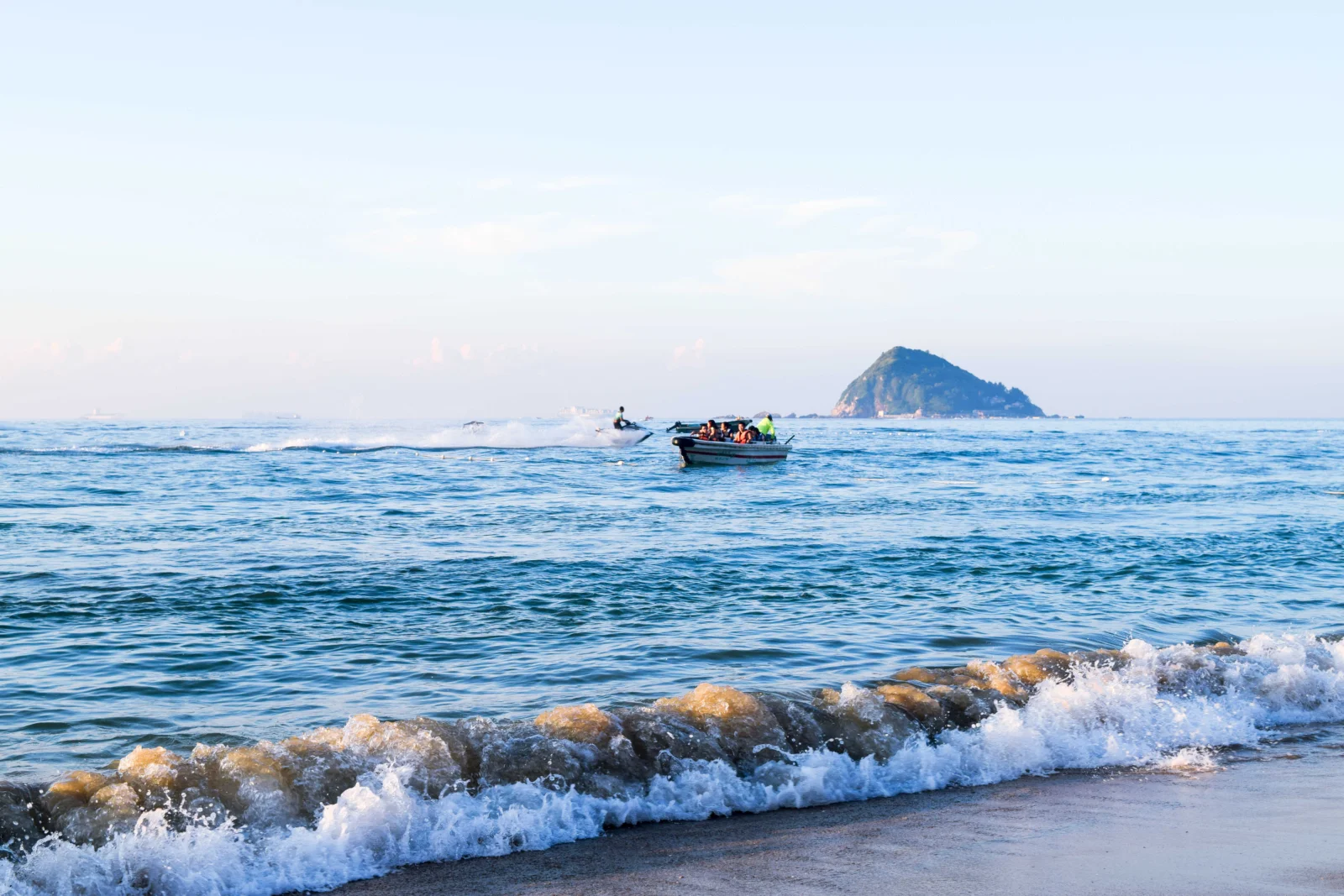 蓝色海面上漂浮着一只小船，远处可见海岛，前景是拍岸的浪花。