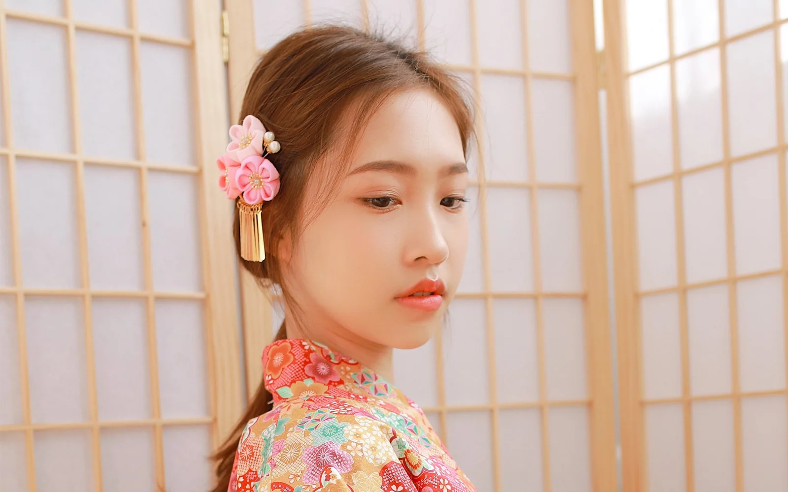 一位身穿彩色传统服饰并佩戴花饰的女性站在木格屏风前。