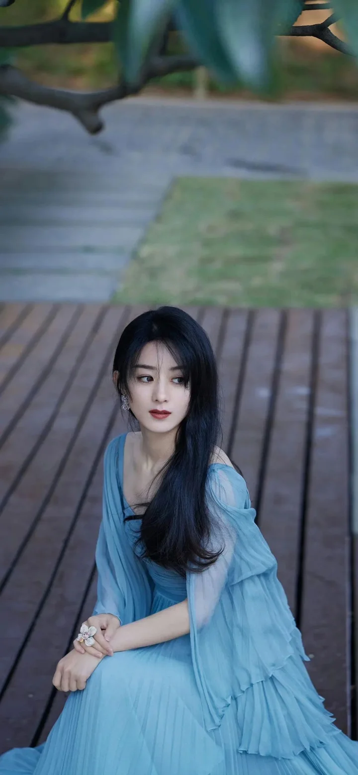 연한 파란색 드레스를 입은 여성이 나무 데크에 앉아 있습니다.