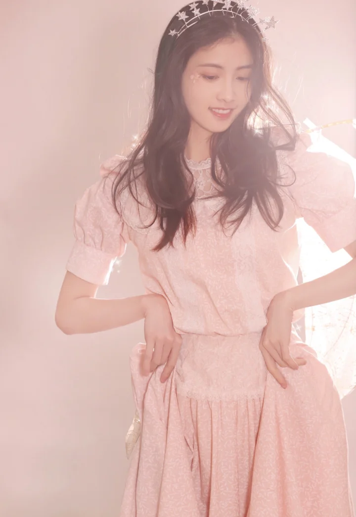 별 장식을 쓴 티아라와 분홍색 원피스를 착용한 여성이 부드러운 빛 속에 서 있습니다.