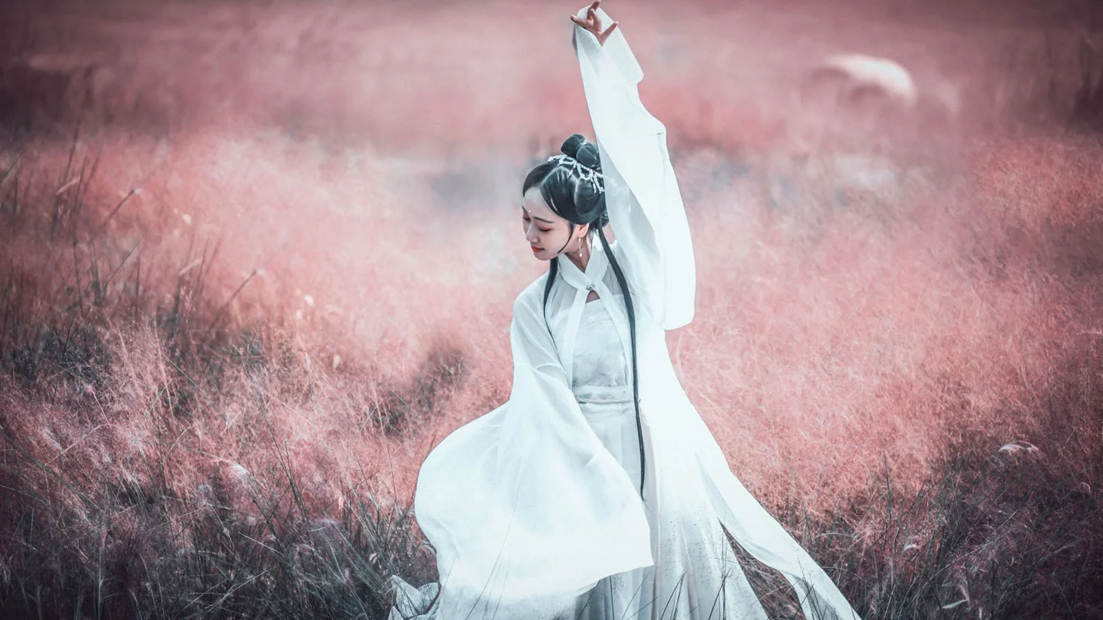 一名身穿白色长袍的女子站在粉色草地中，抬起一只手臂。