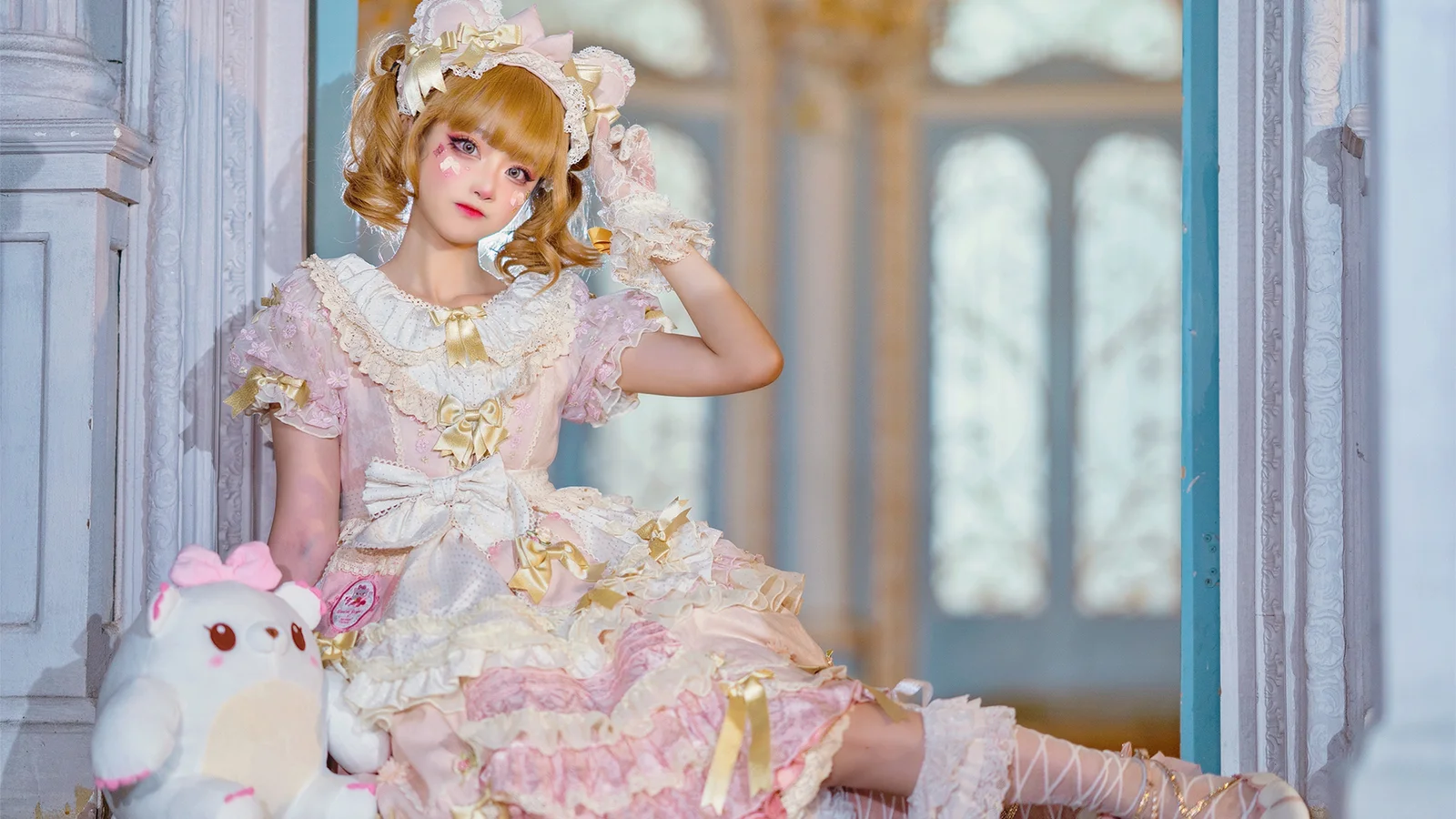 パステルカラーのフリルドレスを着た女性が、白いぬいぐるみのそばで華やかな扉口に座っています。