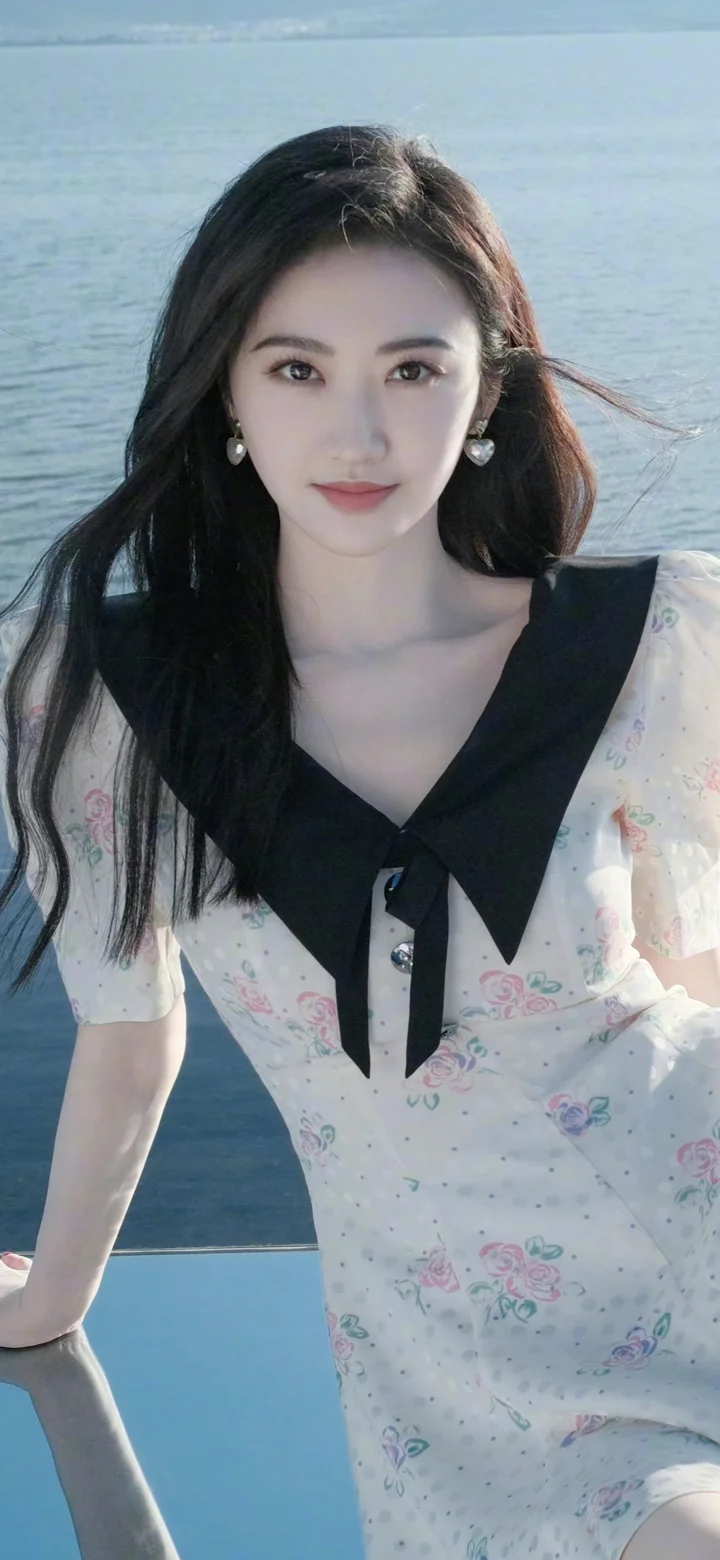 一位成年女性穿着浅色花卉连衣裙站在海边。