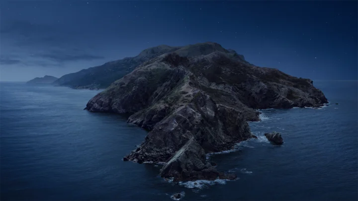 夜色中的崎岖海岛伸入平静的深蓝色海面，天空点缀着稀疏星光。