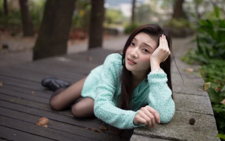 一名成年女性穿着浅绿色毛衣，躺在户外木栈道旁看向镜头。