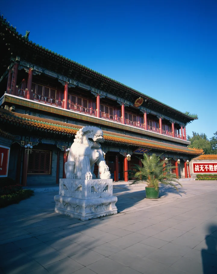 蓝天下，一座彩绘中式古建筑与石狮子坐落在开阔庭院中。