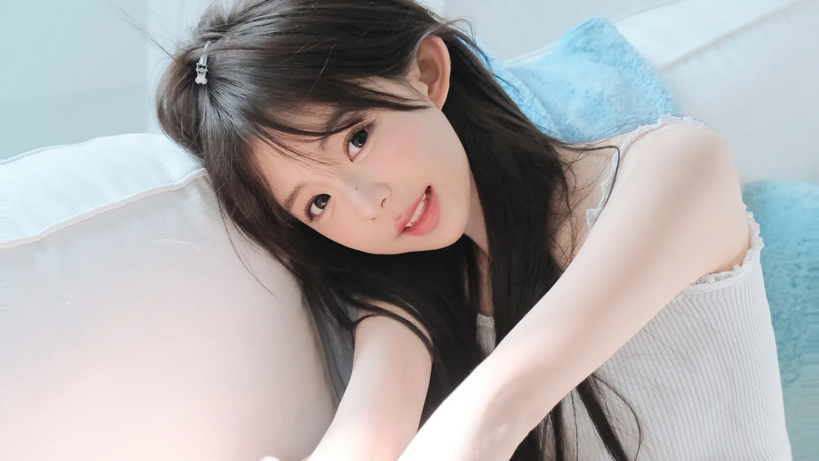 一名长发女性靠在床上，面向镜头微笑。