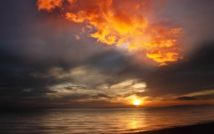 夕阳沉入海平线，橙红色云层映照在平静海面上。