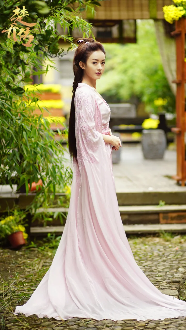 一名身穿粉色传统服饰的女子站在竹子环绕的庭院小径旁。