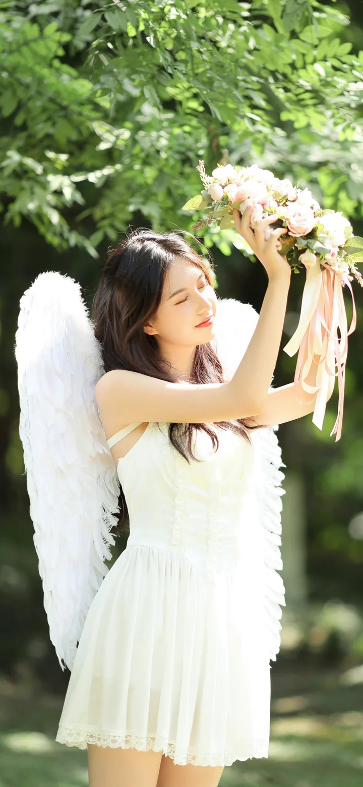 一位身穿白裙、佩戴羽翼的女性在树林中举起花束。