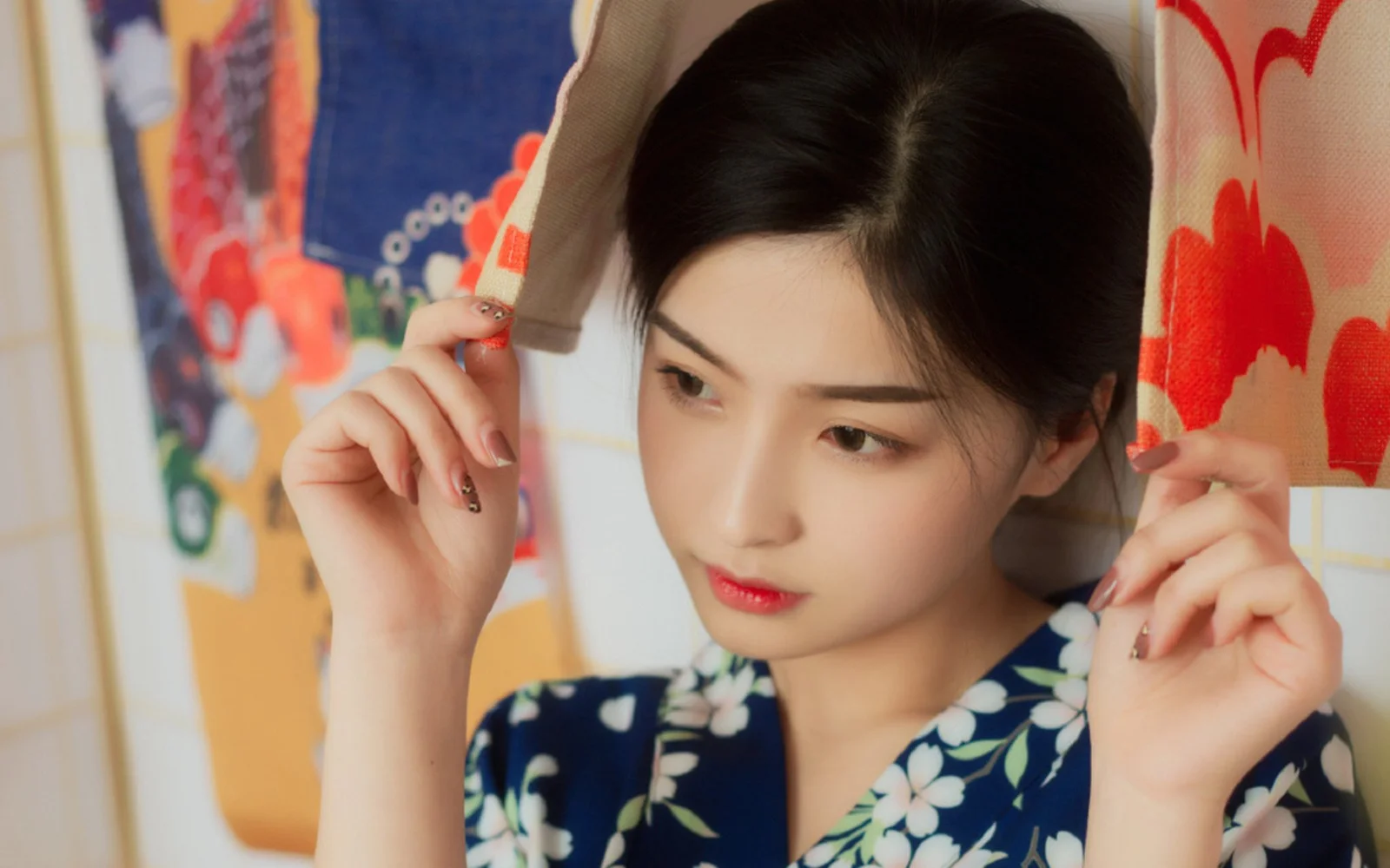青い花柄のワンピースを着た女性が、色鮮やかなカーテンの前で薄い布を手にしています。