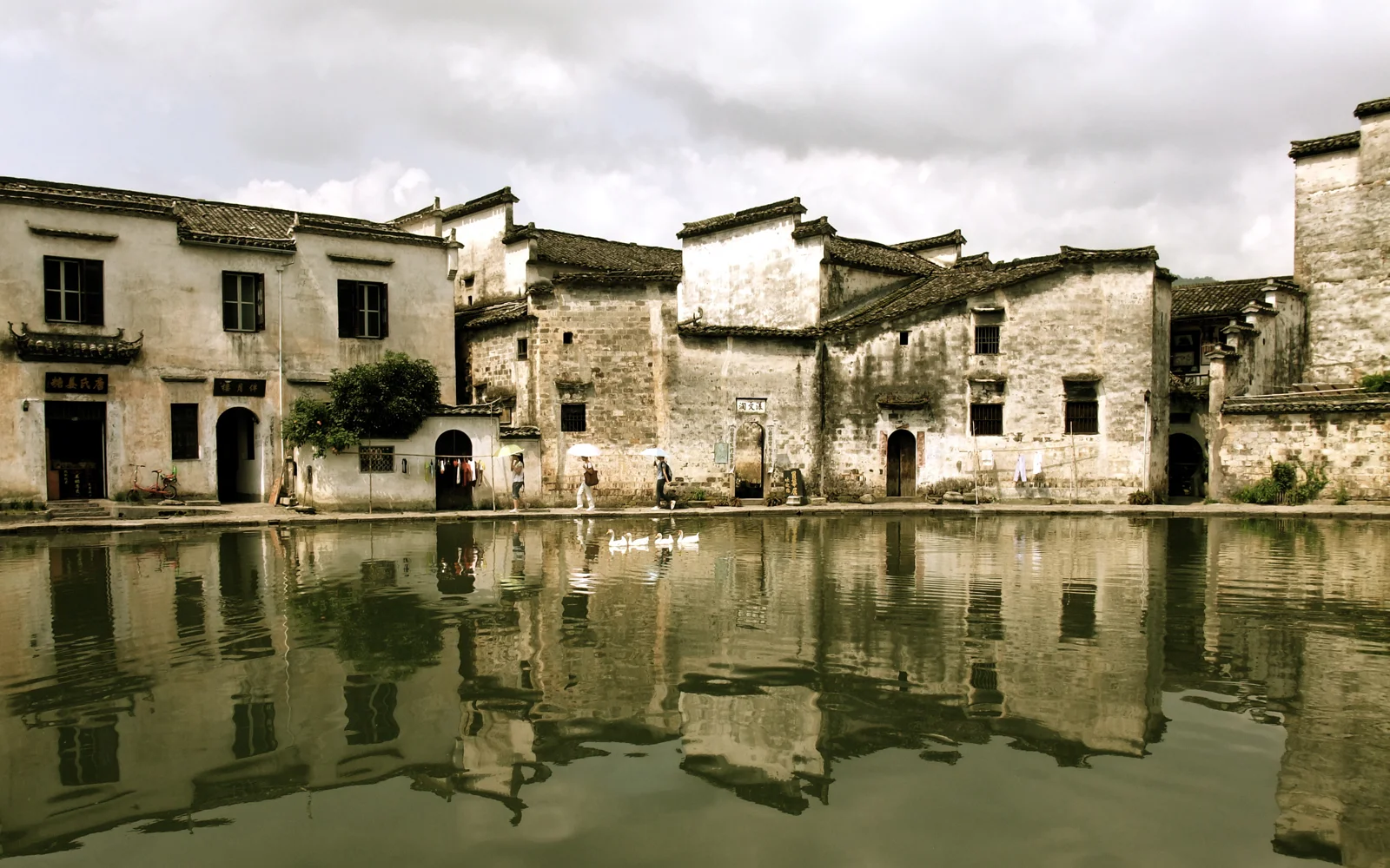 一排古朴的临水建筑倒映在平静的运河中，天空被厚重云层覆盖。