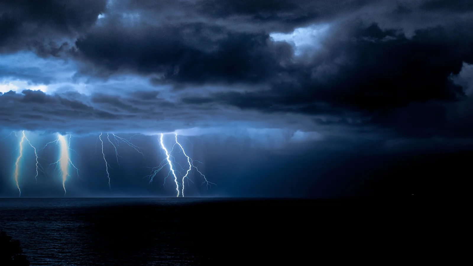 乌云笼罩的海面上闪电划破夜空，呈现出深蓝色的暴风雨景象。