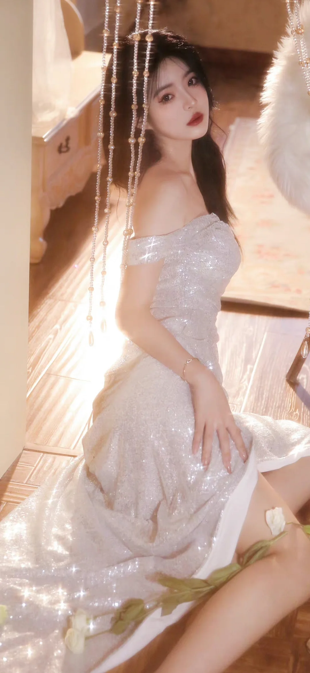 一名成年女性身穿银色闪亮礼服，坐在室内珠帘旁。