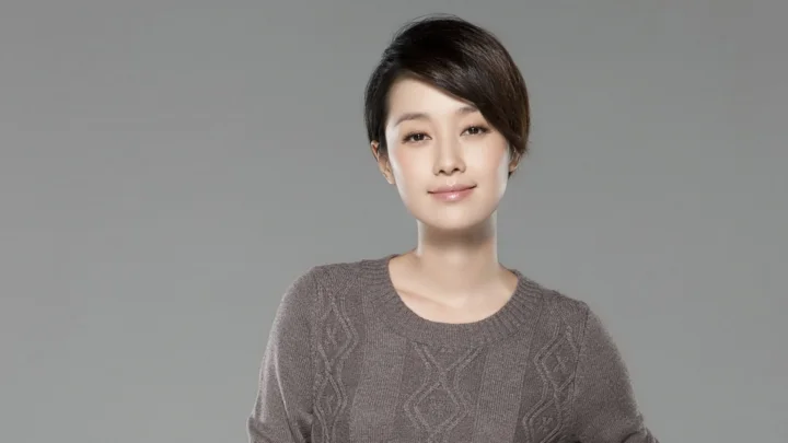 一名成年女性身穿灰色针织衫，在纯灰色背景前面向镜头微笑。