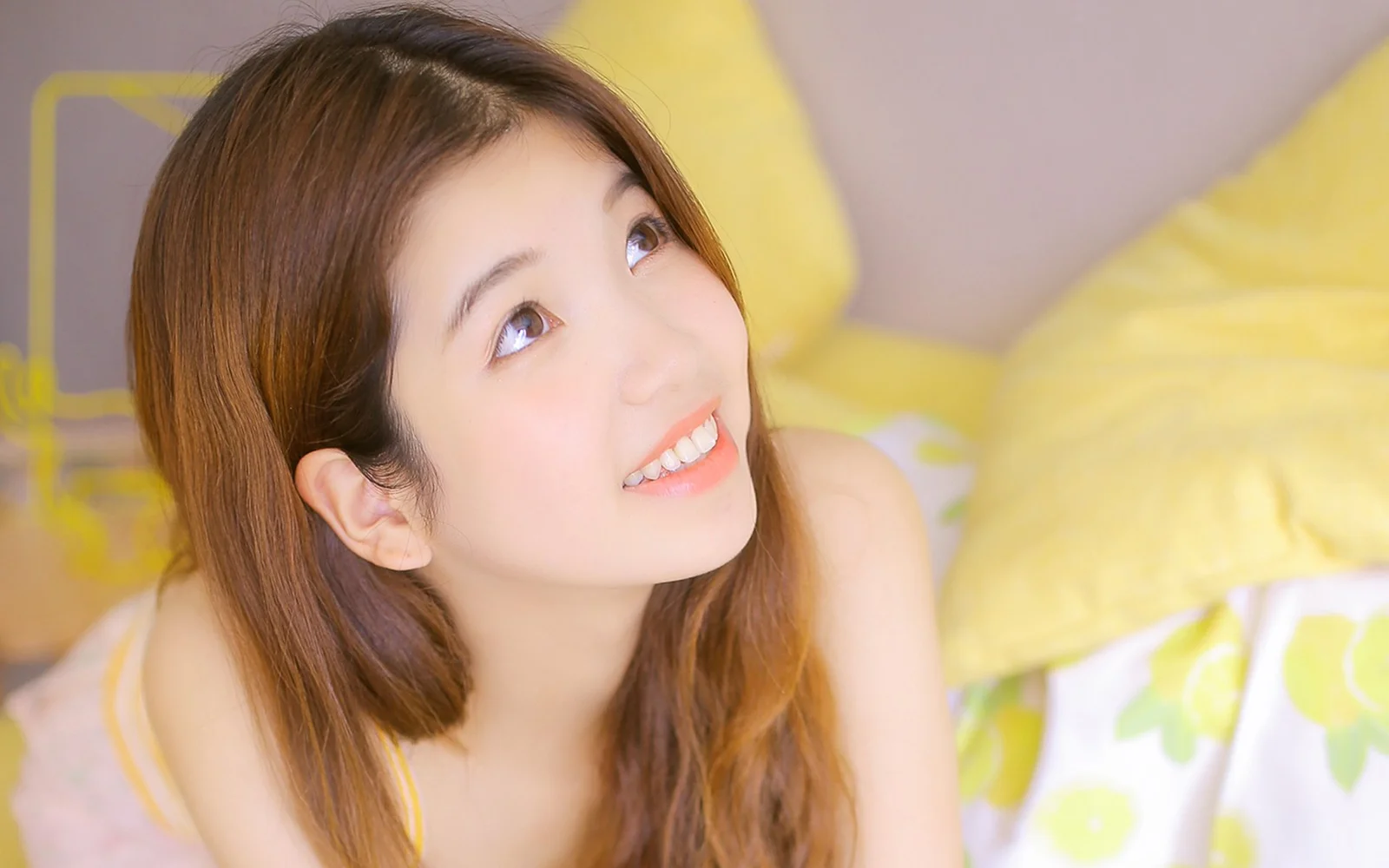 一名棕色長髮女子在明亮的臥室中微笑並抬頭望向一側。
