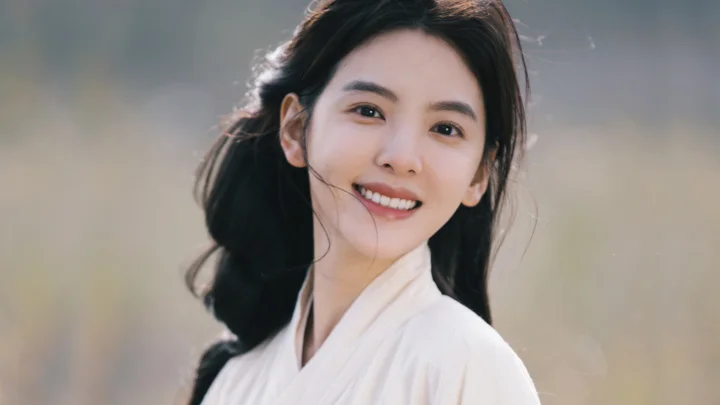 흰색 옷을 입은 성인 여성이 부드럽게 흐려진 배경 앞에서 카메라를 향해 미소 짓고 있다.
