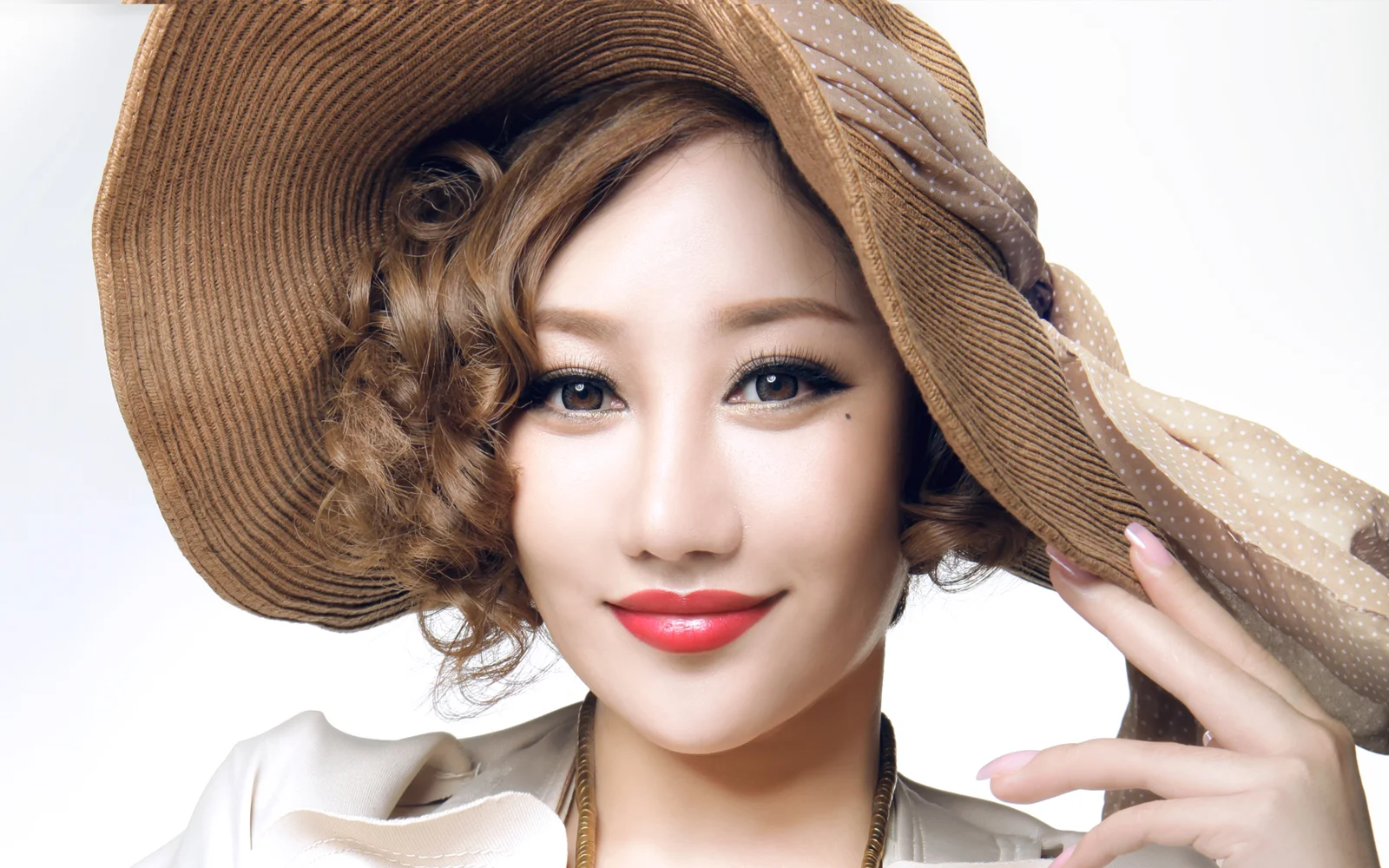 갈색 챙이 넓은 모자와 흰색 상의를 입은 여성이 밝은 배경 앞에서 미소 짓고 있다.