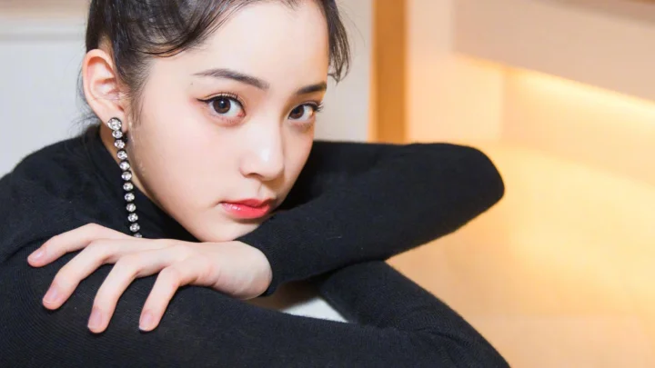 一位身穿黑色毛衣的成年女性靠着手臂面向镜头，背景带有温暖的室内光线。