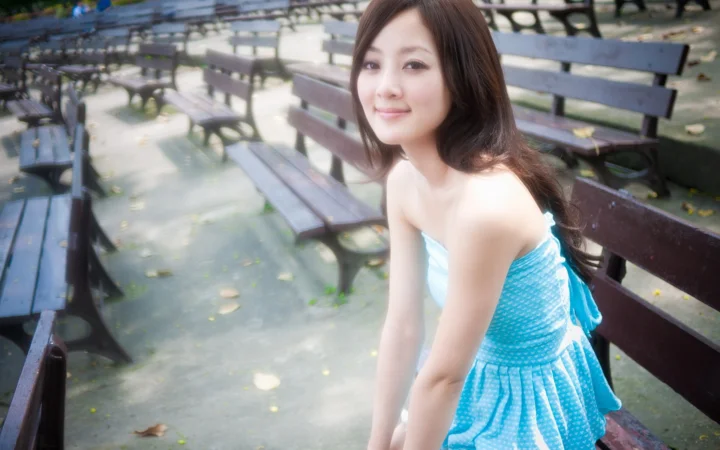 파란색 원피스를 입은 성인 여성이 공원 벤치 옆에 앉아 있습니다.