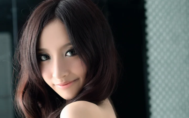 一位棕色长发女性面向镜头微笑，柔和光线突出她的面部轮廓。
