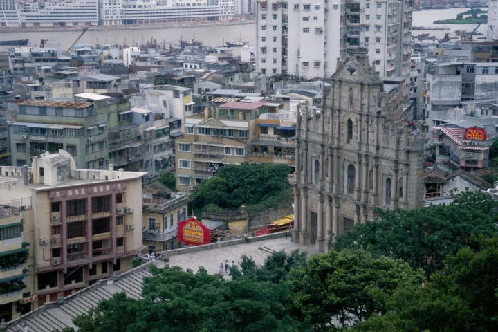 俯瞰澳门密集的城市建筑、绿树与一座历史教堂遗址。