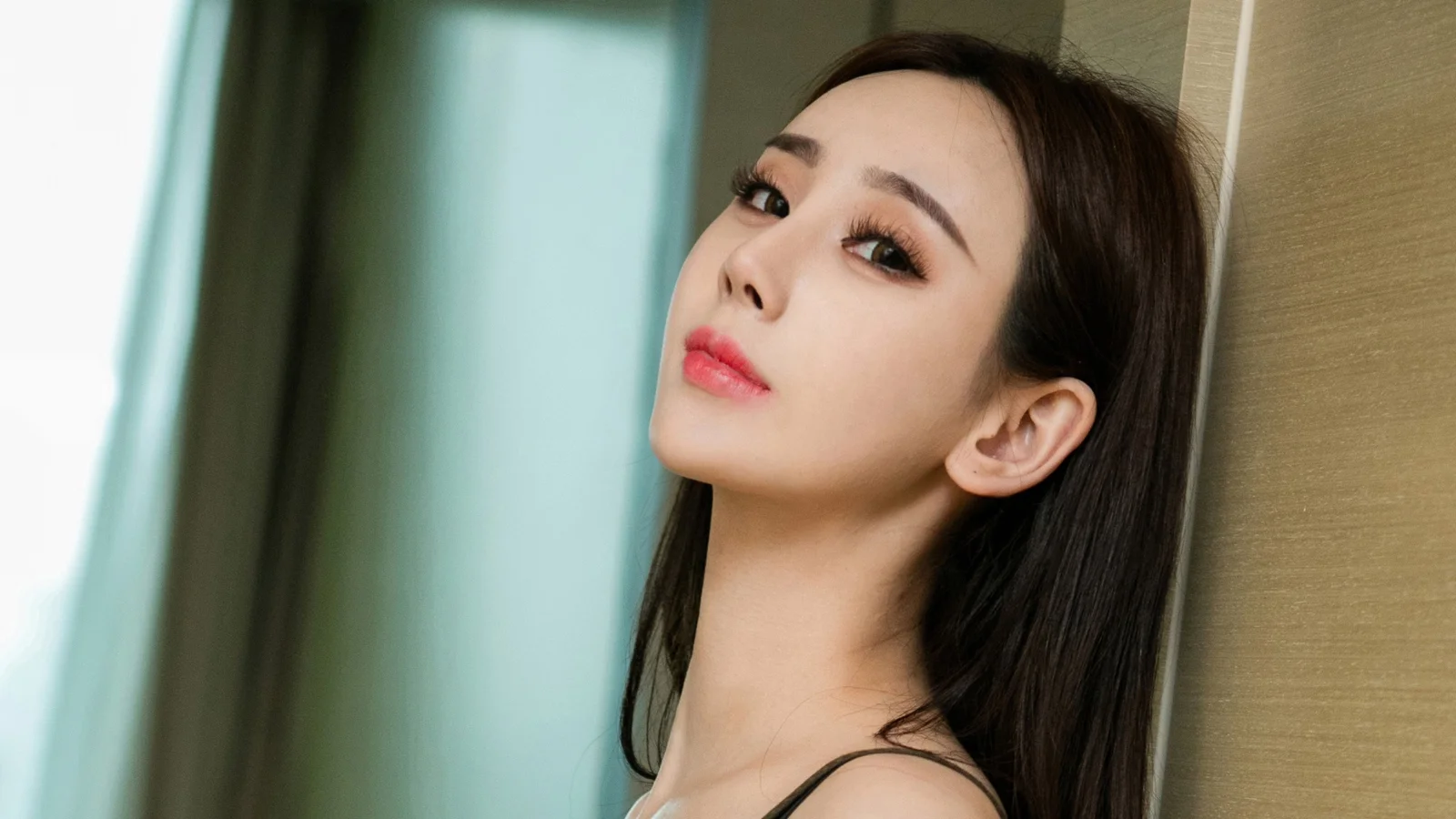 一位长发女性靠在室内墙边，侧头面向镜头。
