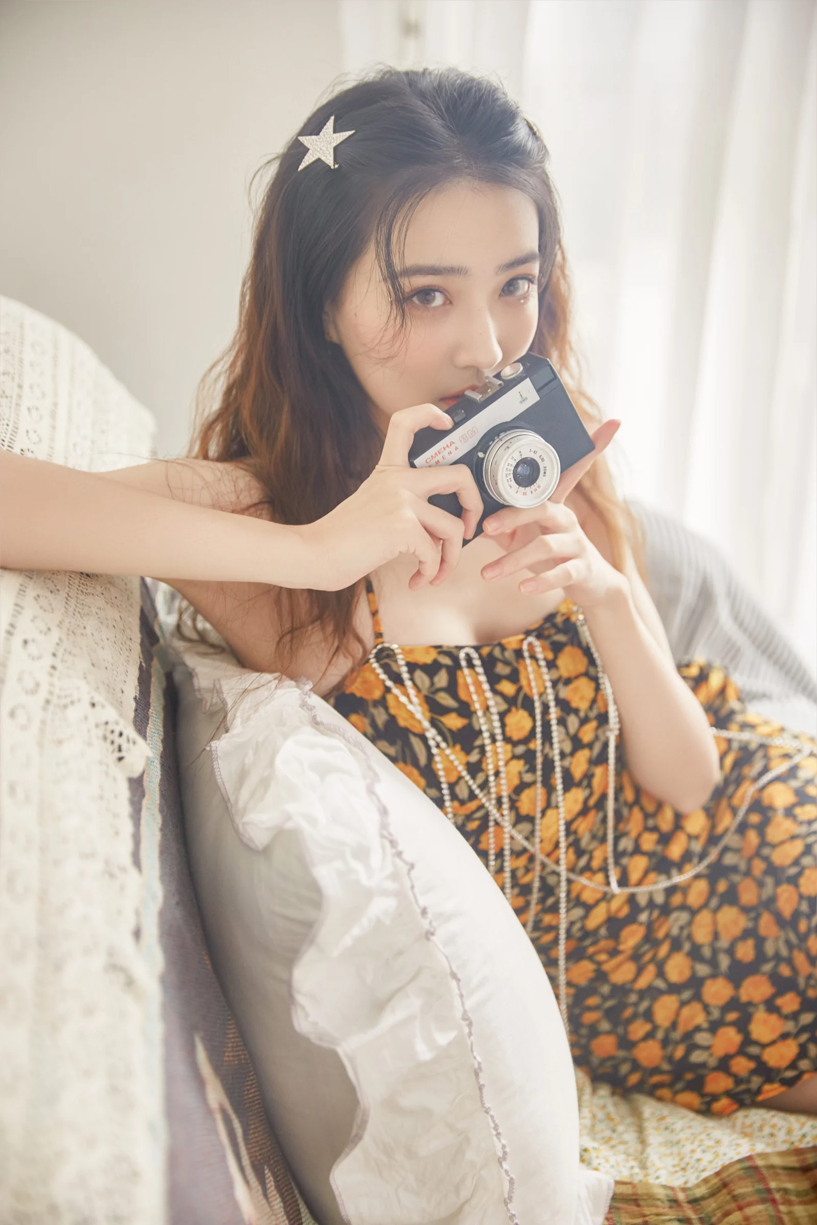 一位女子坐在室内沙发上，手持相机面对镜头。