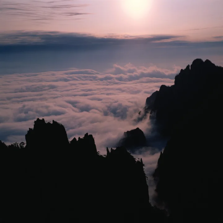 暮色天空下，深色山峰环绕着翻涌的云海。