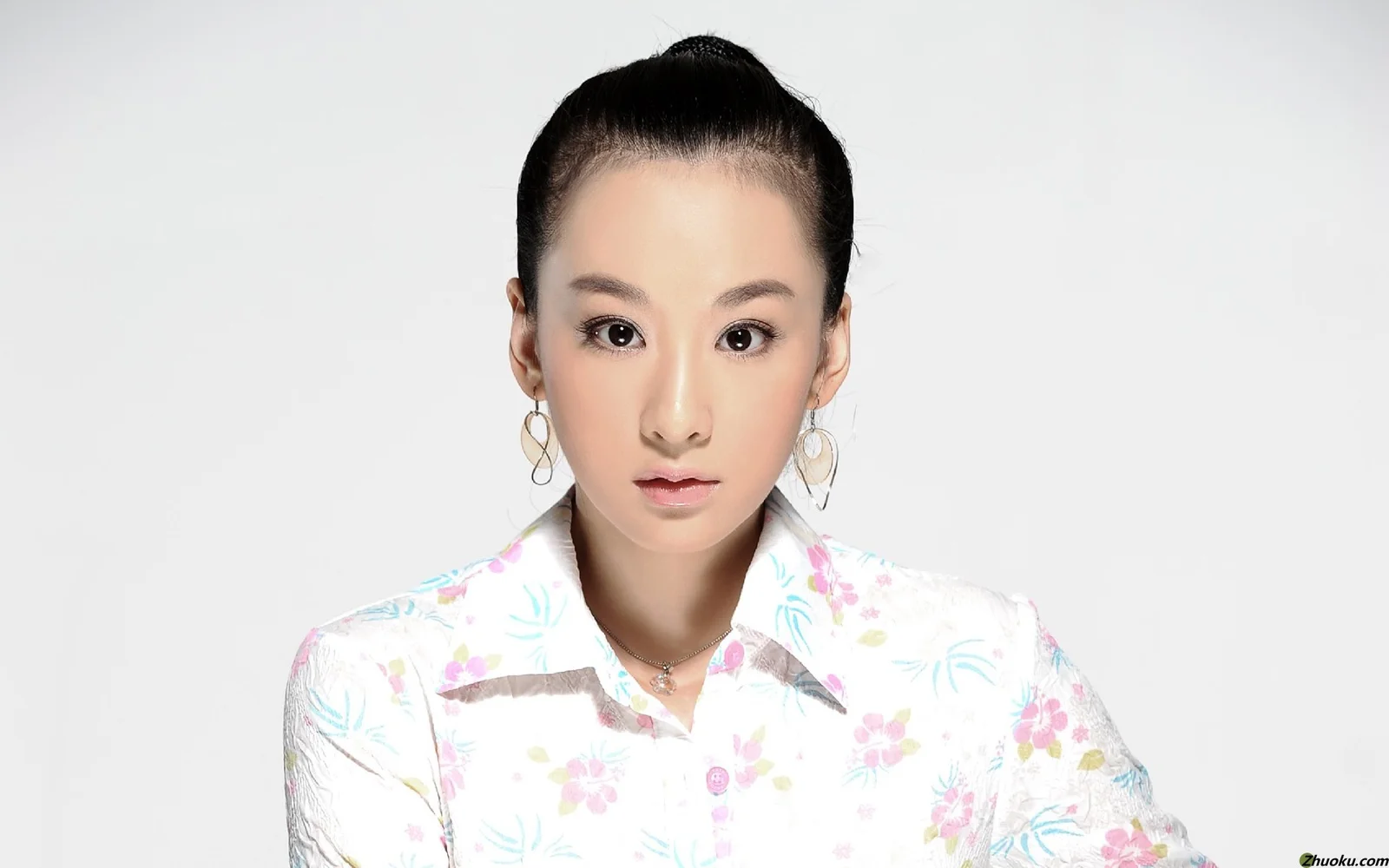 흰색 꽃무늬 셔츠를 입은 성인 여성이 밝은 회색 배경 앞에서 정면을 바라보고 있습니다.