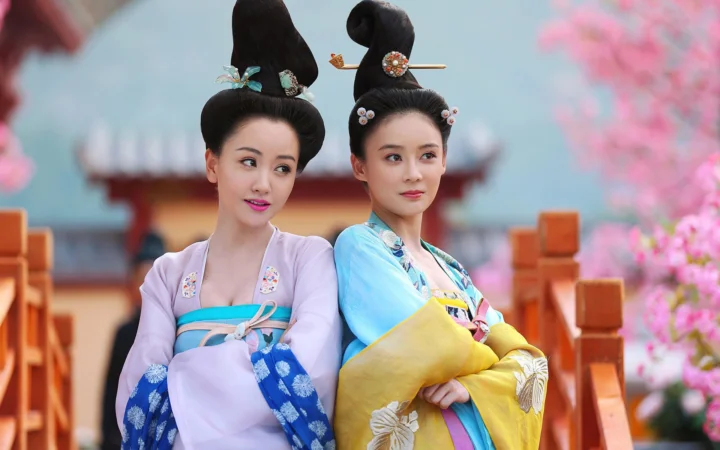 两名身穿传统服饰、梳着 ornate 发髻的成年女性站在庭院花树之间。