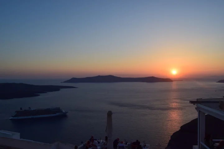 夕阳映照着平静的海面、远处的岛屿轮廓和一艘游船。