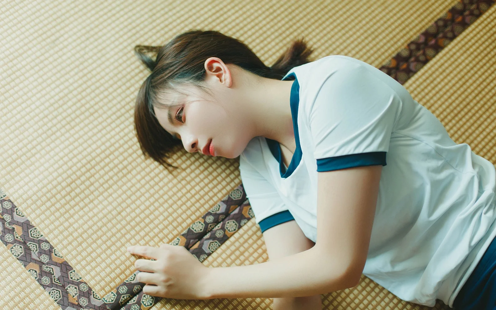 白と青の縁取りのシャツを着た女性が、編み mat の上に横たわっている。