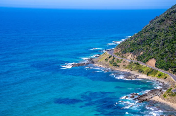 湛蓝海水沿着植被覆盖的海岸延伸，一条蜿蜒公路穿过山坡。