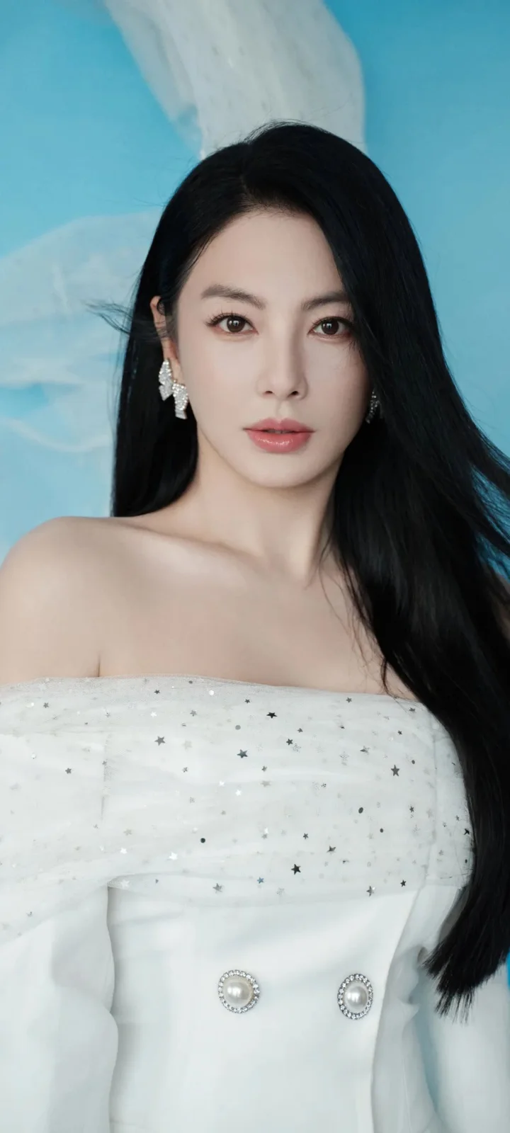 一名黑色长发女性身穿点缀星星图案的白色礼服面对镜头。