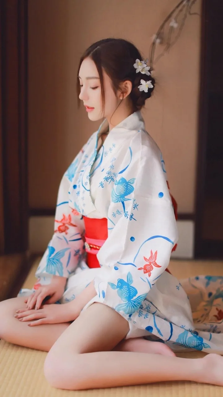 白地に青と赤の花柄の着物を着た成人女性が、室内の畳の上に正座しています。