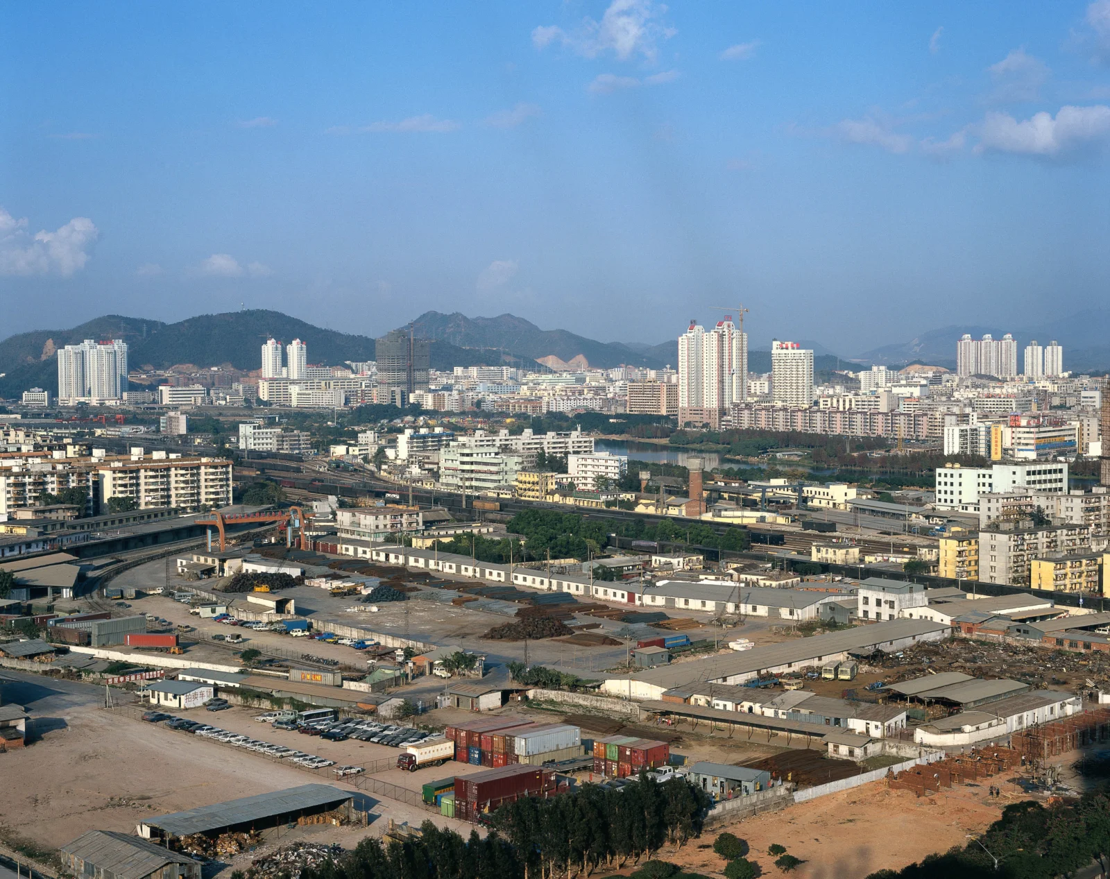 푸른 하늘 아래 도시 건물과 산업 지대, 멀리 보이는 산이 펼쳐진 도시 전경입니다.
