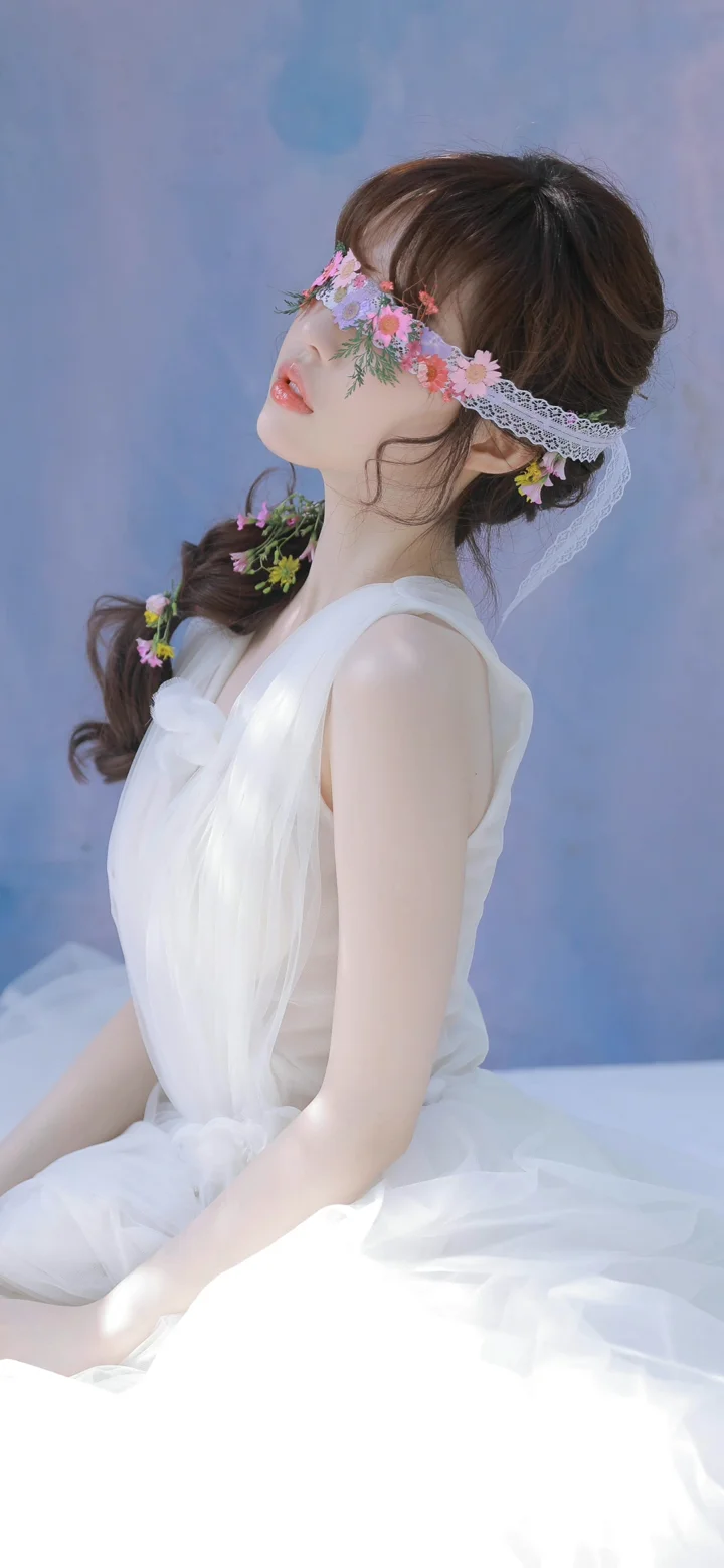 一位身穿白色礼服、佩戴花环的女性在蓝色背景前侧身坐着。