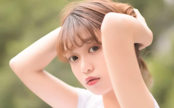 一位棕色头发的女性在柔和的户外背景前抬手整理头发。