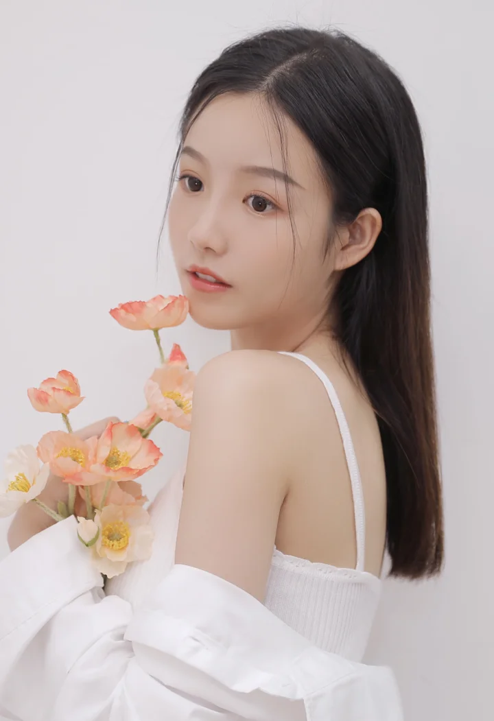 一位长发女性手持粉色花朵回望镜头，背景为浅灰色。