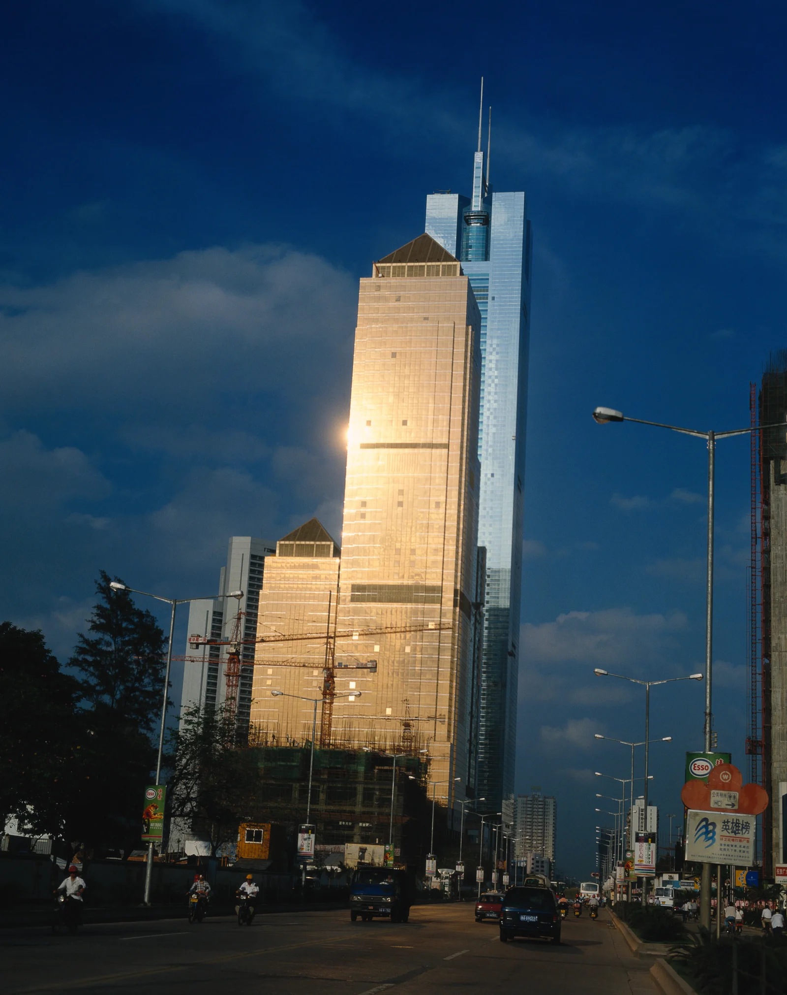 蓝天下的高层建筑矗立在城市街道旁，车辆和路灯延伸向远方。